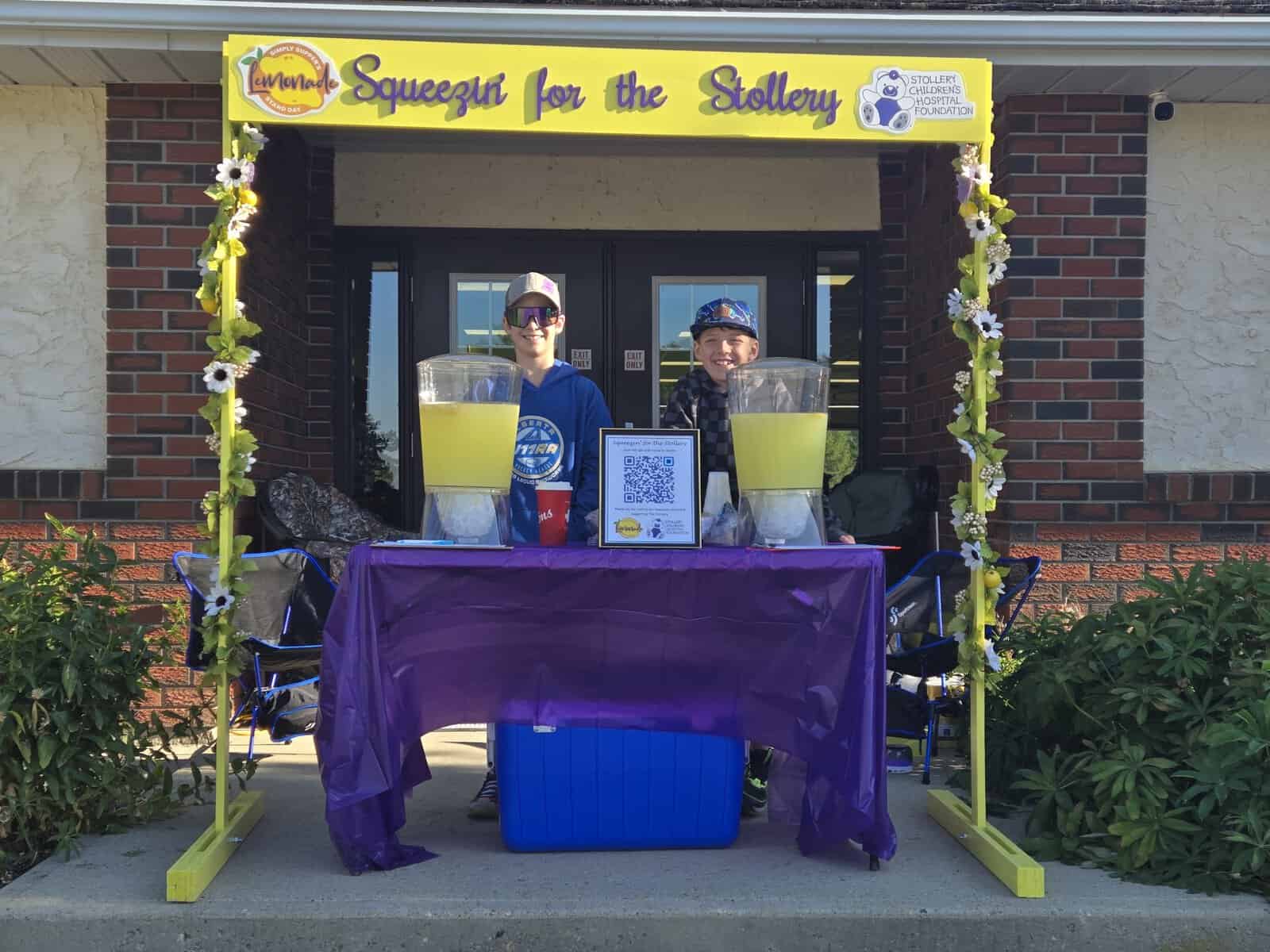 Two volunteers at a lemonade stand for Lemonade Day 2025 supporting the Stollery Children's Hospital, with bright yellow signage and cheerful setup.