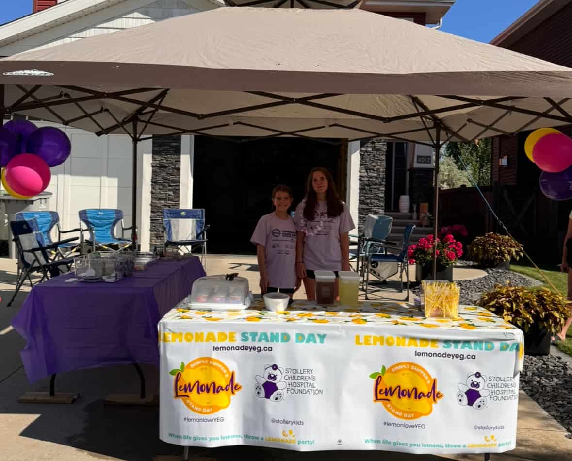 Children at Lemonade Stand Day 2025 event, showcasing a lemonade stand with colorful decorations and banners, promoting community and charity.